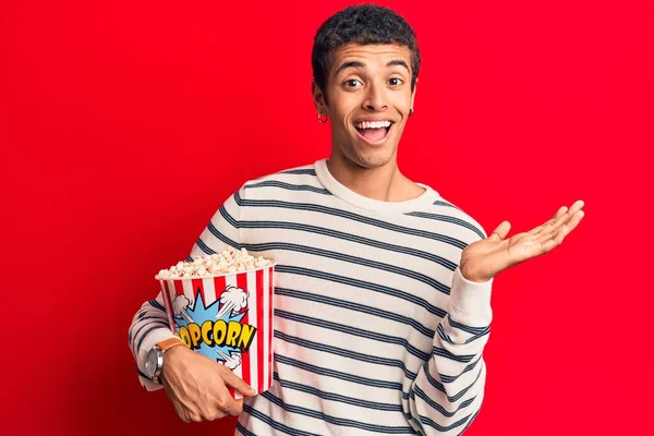 Genç Afrikalı Amerikalı adam elinde patlamış mısırla başarıyı mutlu bir gülümsemeyle kutluyor ve kazanan el kaldırarak ifade ediyor. 