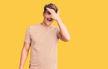 Gündelik kıyafetler giyen ve gözlüklü genç yakışıklı adam şok içinde yüzünü ve gözlerini kapayarak utanmış bir ifadeyle parmaklarının arasından bakıyor.. 