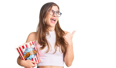 Güzel, beyaz bir kadın elinde patlamış mısırla baş parmağını kaldırmış, ağzı açık gülümsüyor. 