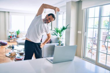 Orta yaşlı, sakallı ve esnek bir adam evde egzersiz yapıyor bilgisayardaki spor videolarına bakıyor.