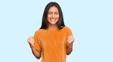 Genç esmer Arap kadın gündelik giysiler giyiyor. Çok mutlu ve heyecanlı. Kazanan jest yapıyor, kollarını kaldırıyor, gülümsüyor ve başarı için bağırıyor. kutlama konsepti. 