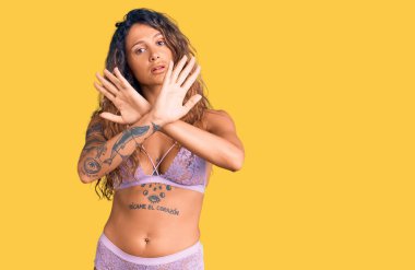 Dövmeli genç İspanyol kadın iç çamaşırı giyiyordu. Reddedilmişti. Kollarını kavuşturuyordu. 