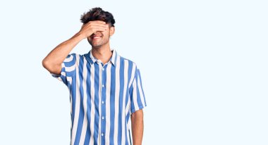 Gündelik kıyafetler giyen, gülümseyen ve gülümseyen genç İspanyol adam şaşırmak için gözlerini kapatıyor. kör kavram. 