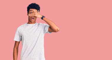 Genç, Afro-Amerikan bir adam günlük giysiler giymiş. Şoka girmiş, yüzünü ve gözlerini kapamış, utanmış bir ifadeyle parmaklarının arasından bakıyor.. 