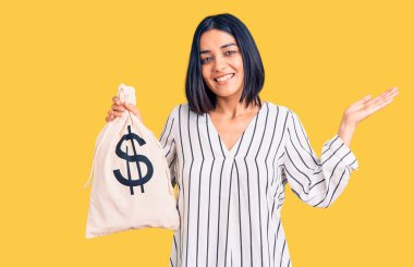 Dolar sembollü para çantası taşıyan genç ve güzel bir Latin kadın zaferi mutlu bir gülümsemeyle kutluyor ve kazanan el kaldırarak ifade ediyor. 