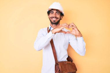 Kıvırcık saçlı yakışıklı genç bir adam ve mimar şapkası takan bir adam. Aşkla gülümseyen, kalp sembolü ve elleriyle şekil veren. romantik kavram. 