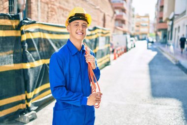 Genç İspanyol işçi gülümsüyor. Şehrin caddesinde elektrik kablosu tutarken mutlu.