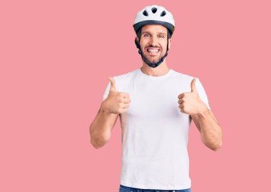 Bisiklet kaskı takan yakışıklı bir adam. Elleriyle olumlu jest yapıyor. Gülümsüyor ve mutlu. Neşeli ifade ve kazanan jest. 