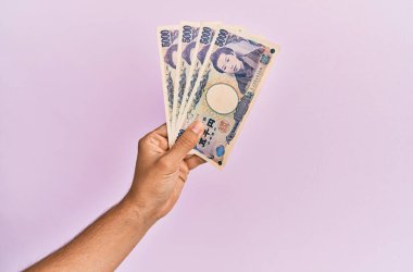 İspanyol eli, izole edilmiş pembe arka planda 5000 Japon doları tutuyor..