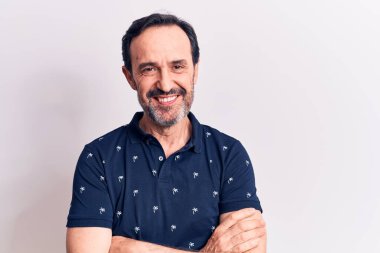 Sıradan polo giyen orta yaşlı yakışıklı bir adam izole edilmiş beyaz arka planda durup kollarını kavuşturup kameraya bakarken gülümsüyor. Pozitif kişi.
