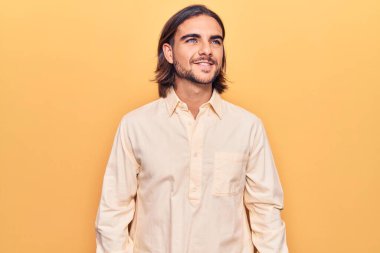 İş kıyafetleri giymiş, yüzünde gülümsemeyle yan yana bakan yakışıklı bir genç. Doğal bir ifade. Kendinden emin gülen. 