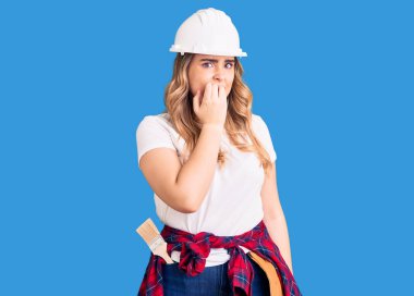 Güvenlik kaskı takan genç beyaz kadın gergin ve gergin görünüyor. Ağzı tırnak yiyen ellerle. anksiyete. 