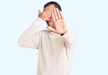 Gündelik kıyafetler giyen, gözlük takan, ellerle gözleri kapayan ve üzgün ve korku ifadeleriyle jest yapan genç yakışıklı bir adam. utangaç ve olumsuz kavram. 