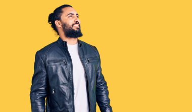 Sıradan deri ceket giyen genç bir Arap yüzünde gülümsemeyle yan yana bakıyor, doğal bir ifade. Kendinden emin gülen. 