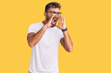 Gündelik kıyafetler ve gözlük takan genç İspanyol adam elleri ağzında kızgın bir şekilde bağırıyor. 