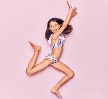 Tatildeki sevimli İspanyol kız bikini giyip ağzı açık gezerken şaşırdı. İzole edilmiş pembe arka plan üzerinden atlama