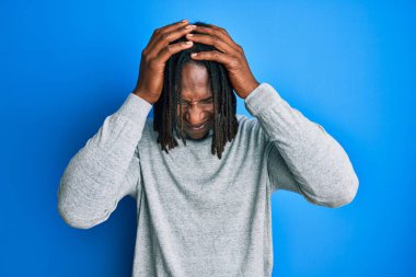 Boğazlı kazak giyen Afrika kökenli Amerikalı bir adam baş ağrısı ve stres yüzünden acı çekiyor çünkü migren ve acı çekiyor. Eller başının üstünde.. 