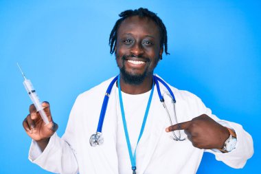 Doktor steteskobu takmış, elinde şırıngayla gülümseyen mutlu ve gururlu birini işaret eden Afrikalı genç bir Amerikalı. 