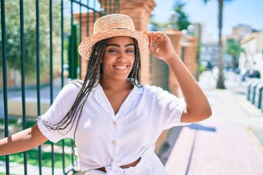 Saçları örgülü, güneşli bir yaz gününde mutlu bir şekilde gülümseyen genç Afrikalı Amerikalı kadın.