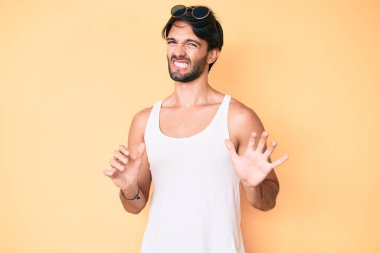 Yaz bakışı ve güneş gözlüğü takan yakışıklı İspanyol adam tiksindirici bir ifade takınıyor ve tiksinti reaksiyonu yüzünden tiksindirici ve korkutucu bir ifade takınıyor. Eller havada. 
