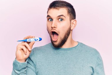 Termometreyi tutan yakışıklı genç adam korkmuş ve ağzı açık kalmış, şaşırmış ve şaşırmış. 