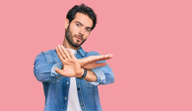 Gündelik kıyafetler giyen genç İspanyol adam. Reddedilmiş yüz ifadesi. Kollar ve avuçlar çapraz. 