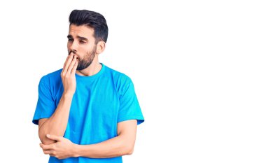 Sıradan tişörtler giyen sakallı genç yakışıklı adam ağzıyla esnemekten sıkılmış. Huzursuz ve uykulu.. 