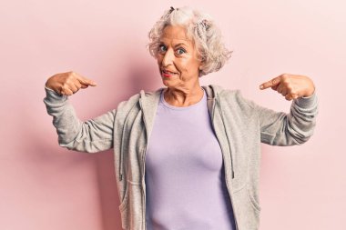 Yaşlı, gri saçlı, günlük spor giysiler giyen, kendine güvenen, gülümseyen, kendini gururlu ve mutlu gösteren bir kadın.. 