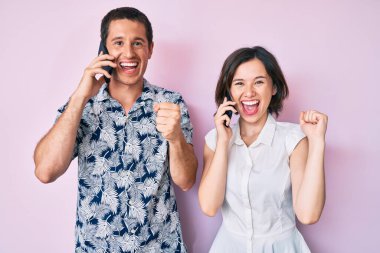Akıllı telefonda konuşan güzel bir çift gururla bağırıyor, zaferi kutluyor ve kollarını kaldırarak başarıyı kutluyor. 