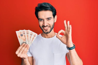 İspanyol asıllı genç adam, elinde 10 pound tutuyor. Banknotlar, tamam imzasını atıyor. Parmaklarıyla imzalıyor. 