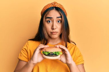 Lezzetli, klasik bir burger yiyen genç Latin kadın şüpheci ve gergin, sorun yüzünden surat asıyor. negatif kişi. 