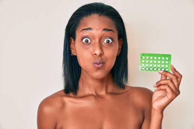 Genç Afrikalı Amerikalı kadın doğum kontrol hapları tutuyor. Komik suratlı yanakları şişiriyor. Ağzı havayla şişer, havayı yakalar.. 