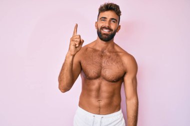 Genç İspanyol adam tişörtsüz duruyor ve bir numarayı gösterip gülümserken kendinden emin ve mutlu.. 