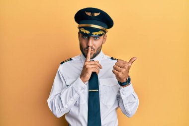 Uçak pilotu üniforması giyen yakışıklı İspanyol adam sessiz olmak istiyor. Parmakları dudaklarında, elleri yandan işaret ediyor. sessizlik ve gizli konsept. 