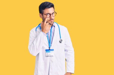 Doktor üniforması giyen ve steteskop takmış genç İspanyol adam jestini ve şüpheli ifadesini izleyerek gözüne işaret ediyor. 