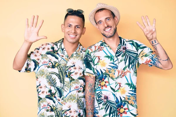 Genç eşcinsel çift, yaz şapkası ve Hawaii tişörtü takıp dokuz numaralı parmaklarını göstererek mutlu ve kendinden emin bir şekilde gülümsediler.. 