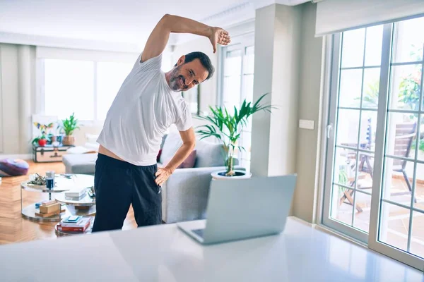 Orta yaşlı, sakallı ve esnek bir adam evde egzersiz yapıyor bilgisayardaki spor videolarına bakıyor.