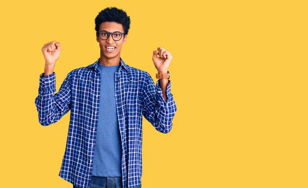 年轻的非洲裔美国人 身穿休闲装 戴着眼镜 高举双臂 睁大眼睛 庆祝成功 获奖者概念 — 图库照片