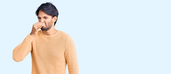 気まぐれなセーターを着たハンサムなヒスパニック系の男性は 臭いと嫌な 耐え難い匂いを嗅ぎ 鼻の上に指で息を保持します 臭いが悪い — ストック写真