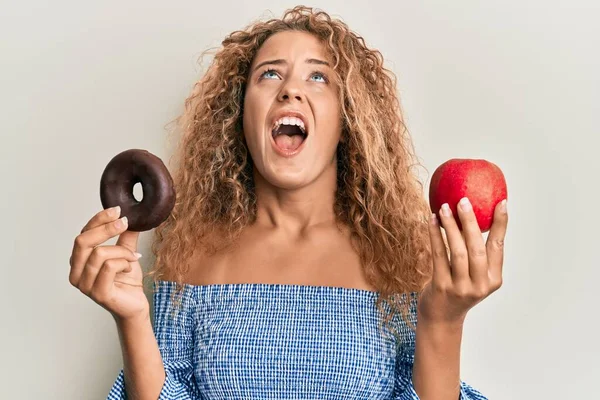 Hermosa Chica Adolescente Caucásica Sosteniendo Manzana Roja Donut Enojado Loco — Foto de Stock