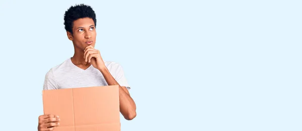 Young African American Man Holding Banner Cardboard Serious Face Thinking — Stock Photo, Image