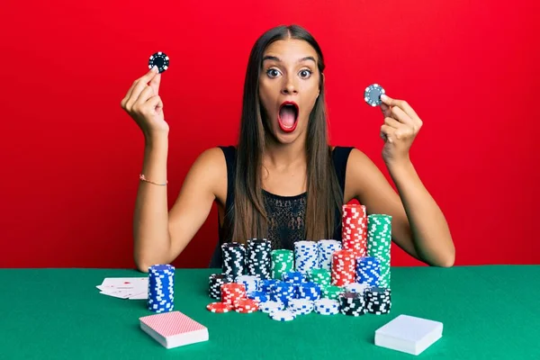 Jovem Hispânica Sentada Mesa Segurando Fichas Cassino Com Medo Chocado — Fotografia de Stock