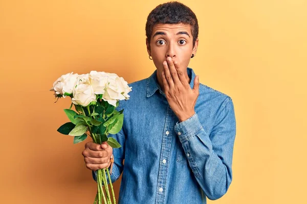 Νεαρός Αφροαμερικάνος Που Κρατάει Λουλούδια Στο Στόμα Χέρι Σοκαρισμένος Και — Φωτογραφία Αρχείου