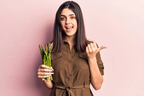 Young Beautiful Girl Holding Asparagus Pointing Thumb Side Smiling Happy — ストック写真