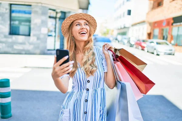 年轻美丽的购物者高兴地微笑着 拿着购物袋走进商店 用智能手机快乐地微笑着 — 图库照片