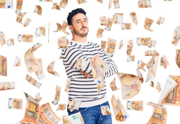 Sıradan kıyafetler giyen genç İspanyol adam kollarını kavuşturmuş ve kendinden emin bir şekilde yan tarafa bakıyor.