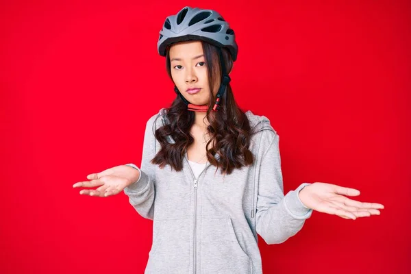 若い美しい中国の女の子は腕や手と自転車のヘルメット無慈悲で混乱表現を着て調達した 疑わしい概念 — ストック写真