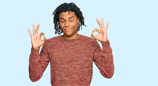 カジュアルな冬のセーターを着た若いアフリカ系アメリカ人の男性は 指で瞑想のジェスチャーをして閉じ目でリラックスして笑顔 ヨガのコンセプト — ストック写真