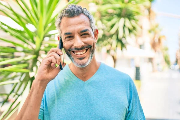 Orta yaşlı, kır saçlı, akıllı telefondan konuşan bir adam şehrin caddesinde yürüyor..