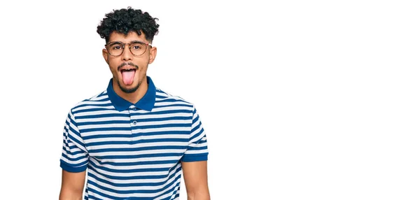 年轻的阿拉伯男子穿着休闲装 戴着眼镜 带着滑稽的表情高兴地伸出舌头 情感概念 — 图库照片